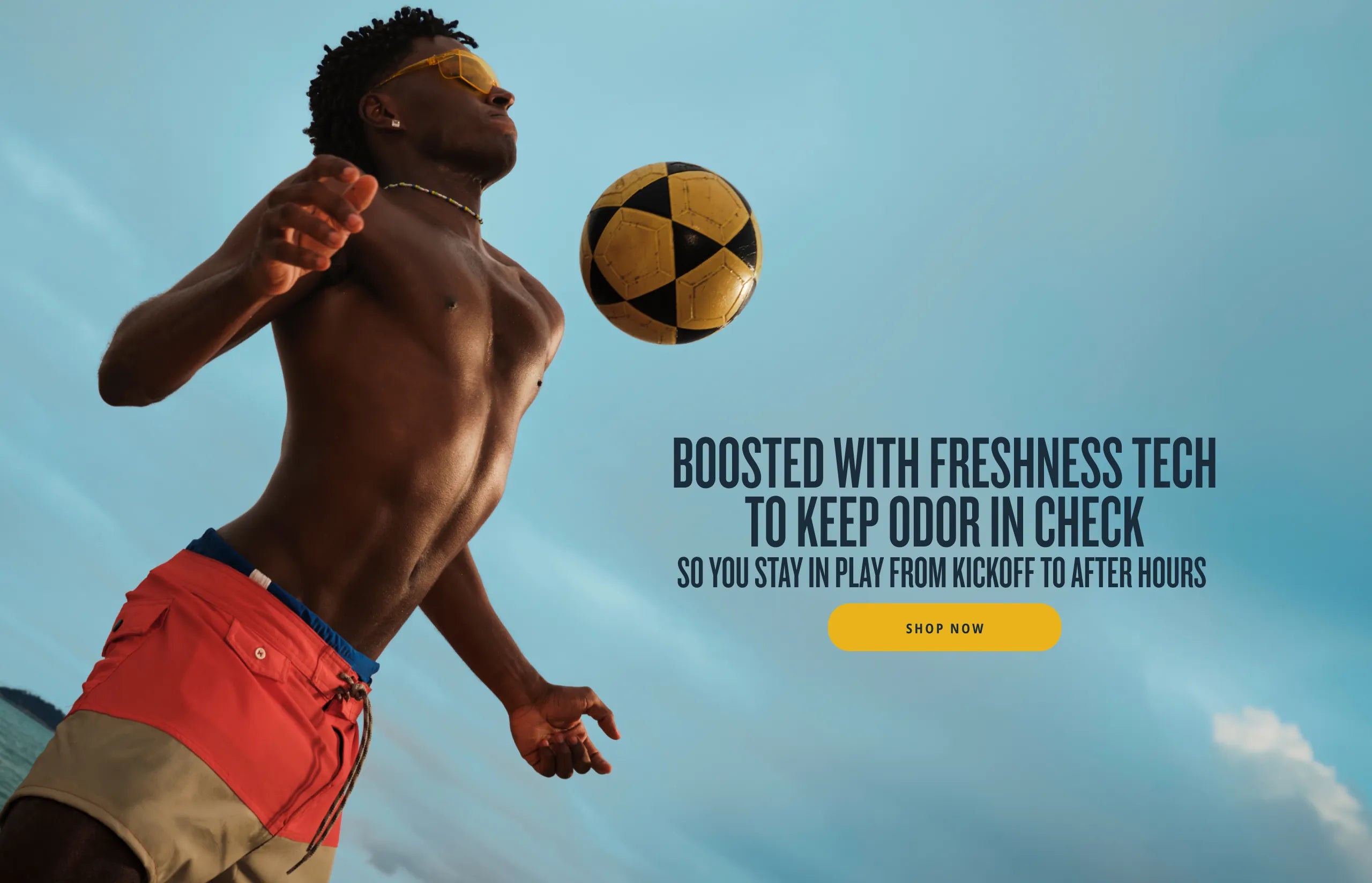 A shirtless man in swim trunks and yellow sunglasses looks up at a yellow and black soccer ball mid-air against a blue sky. Text reads: 'BOOSTED WITH FRESHNESS TECH TO KEEP ODOR IN CHECK SO YOU STAY IN PLAY FROM KICKOFF TO AFTER HOURS' with a yellow Shop Now button.